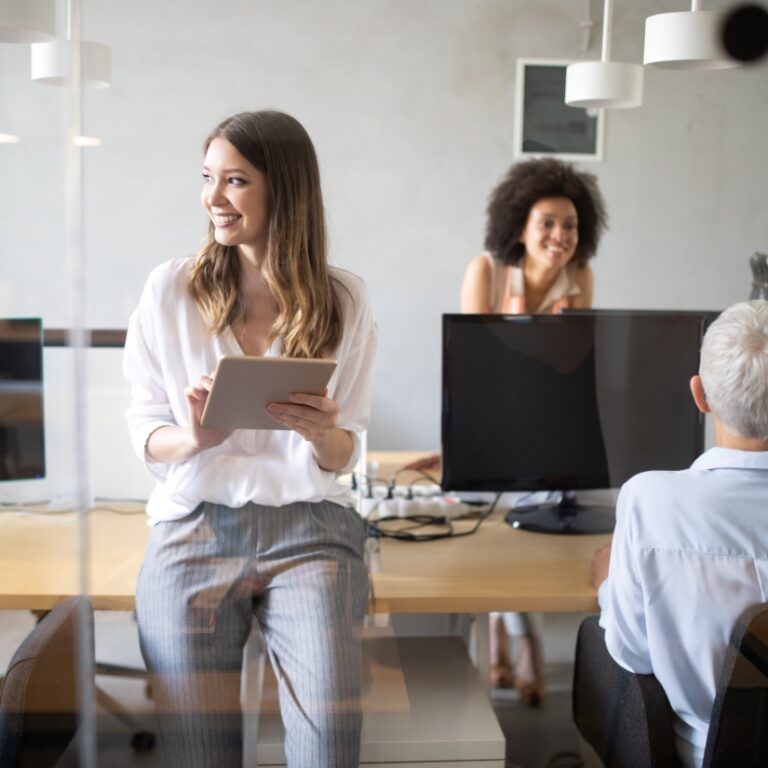 Frau mit Tablet sitzt auf Tischkante und schaut lächelnd zur Seite