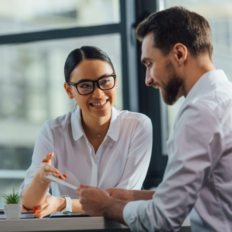 Frau und Mann im Gespräch, er hält ein Dokument zum Unternehmensverkauf in der Hand