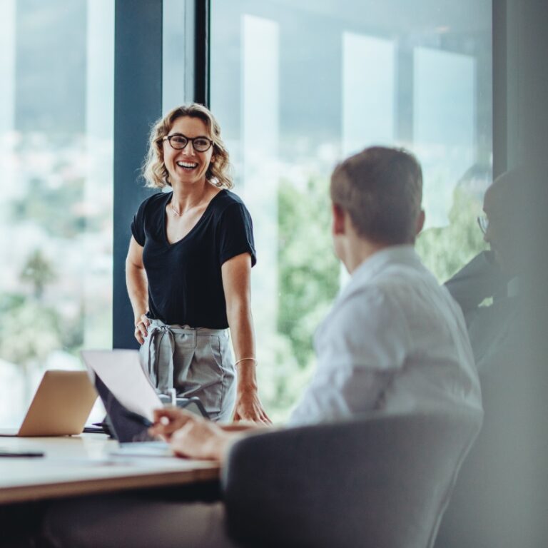 Meeting zum Unternehmensverkauf, Frau steht am Tisch und lacht