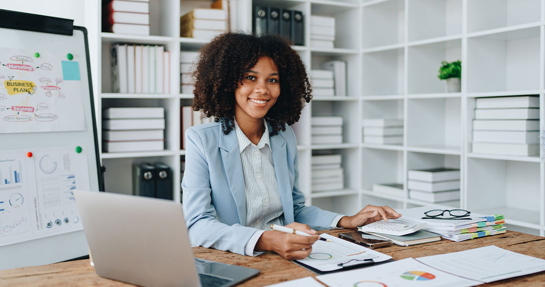 Frau am Tisch mit Unterlagen und Taschenrechner symbolisiert Unternehmensfinanzierung